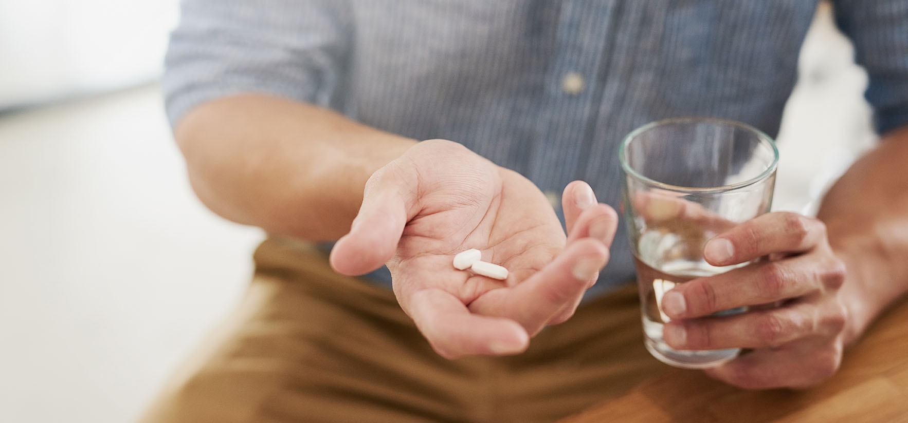Closeup shot of an unrecognisable man holding a glass of water and medication in his hands