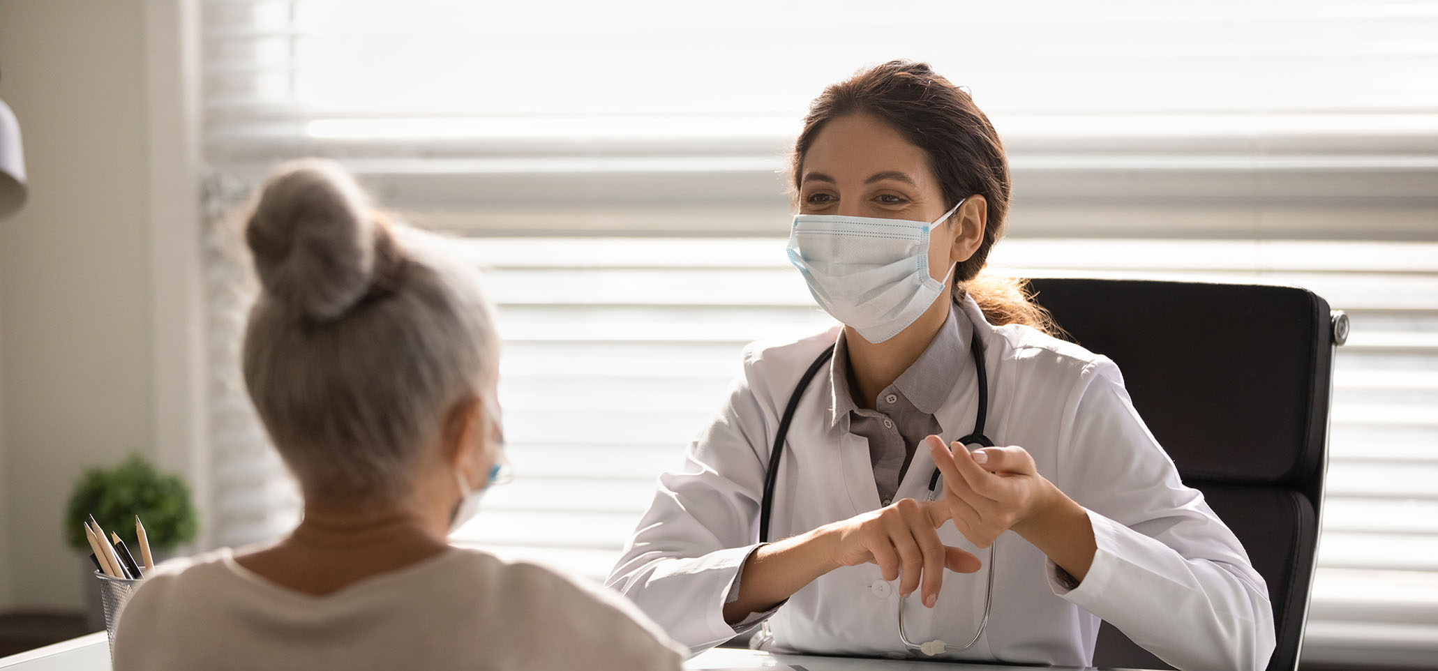 Female doctor in medical facial mask have consultation with elderly patient during covid-19 pandemics. Woman GP in facemask talk consult mature client in clinic or hospital. Coronavirus concept.