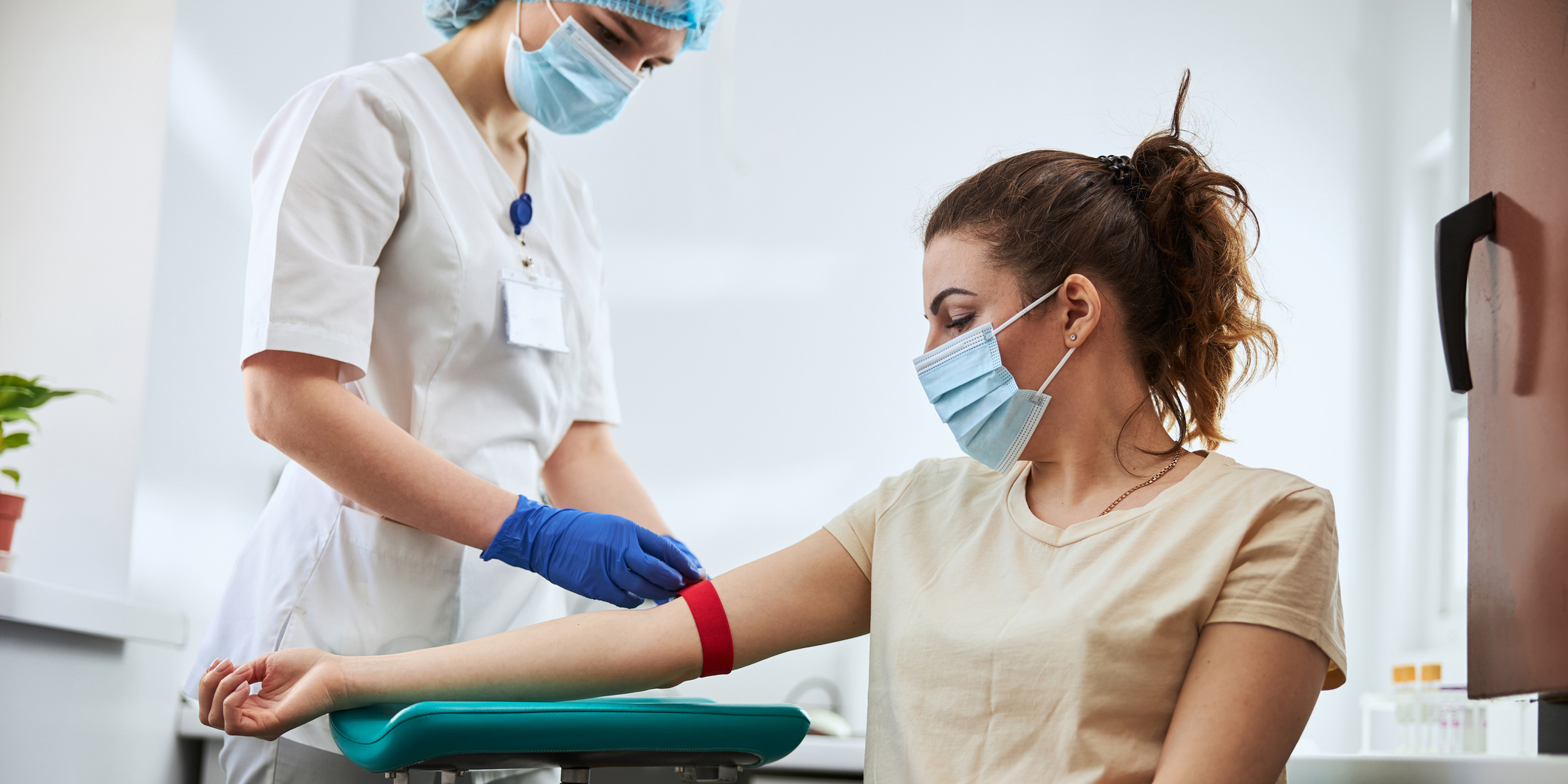 Skilled focused young phlebotomy technician applying a tourniquet to a female patient arm for venipuncture