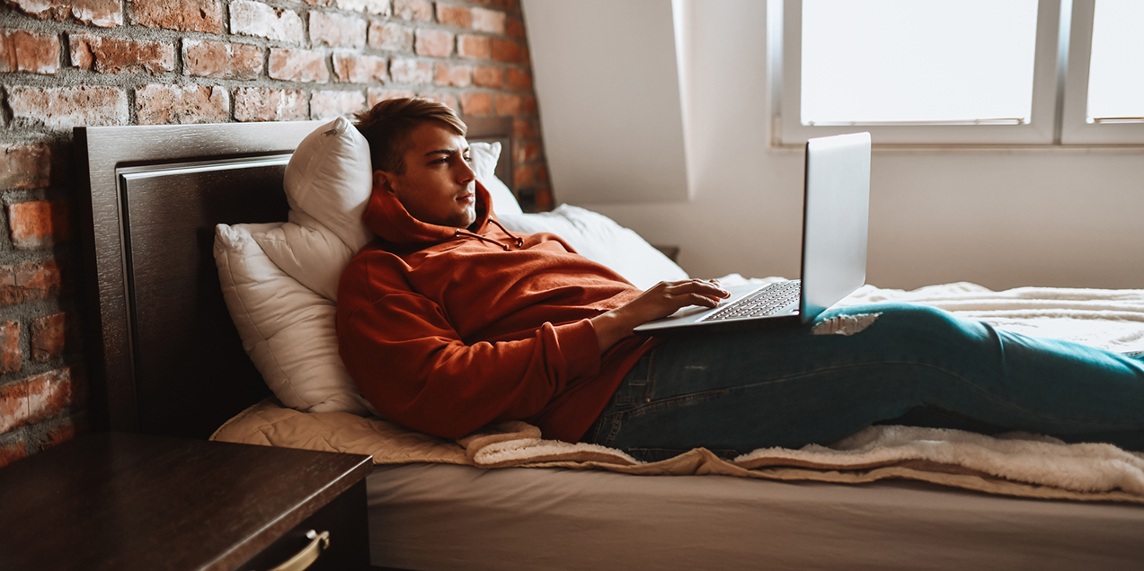 Modern Male Using Laptop While Relaxing In Bed