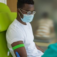 Young man on blood donation at medical clinic, nurse and him are wearing protective face masks for protection against coronavirus