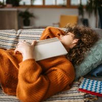 Young pretty student woman napping on the sofa in her living room after studying