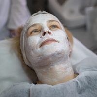 Visiting the beauty salon a woman is lying down wearing a white face mask treatment