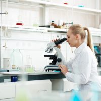 Young woman in white-coat studying new virus in microscope