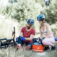 Woman giving first aid to a man with knee injury while cycling on the mountain bicycles on the forest road during the summer time